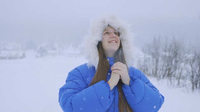 穿着蓝色外套的女人欣赏真正的冬季童话，在大雪中漫步在斯堪的纳维亚村庄