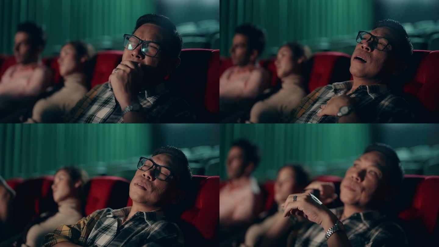 昏昏欲睡的亚洲男子在电影院看无聊的电影时打盹。