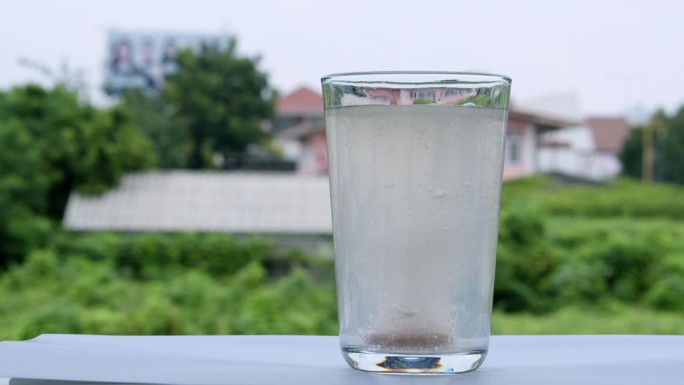 一杯由抗酸剂或碳酸氢钠稀释而成的气泡水，在房屋和绿色植被的背景下出现。