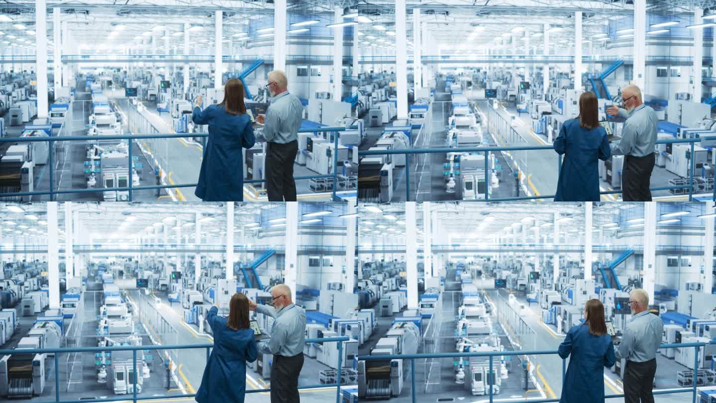 在一家配备人工智能机械臂的现代自动化电子制造工厂，男工程师和女项目经理站在平台上交谈，使用笔记本电脑