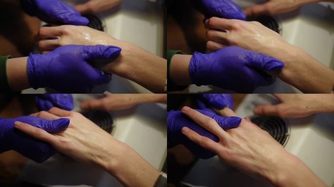 女性双手戴手套按摩男性手掌搓揉润肤霜。特写高视角，无法辨认的高加索美容师在室内美容院为客户服务。