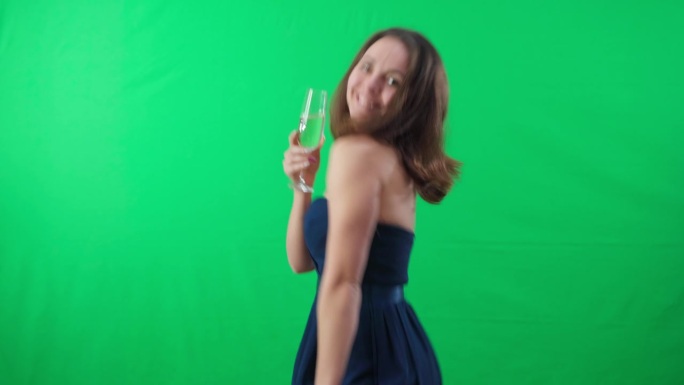 微笑自信的年轻女子的肖像在绿幕背景下跳舞，喝着香槟。快乐、无忧无虑的高加索女士穿着优雅的衣服，在铬m