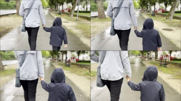 在一个阴雨的日子里，母亲和年幼的儿子手牵着手，裹着暖和的衣服，沿着林荫道和老建筑旁边的人行道散步