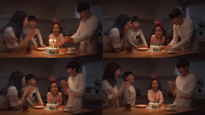 可爱的韩国家庭在晚上用蛋糕和蜡烛庆祝生日。小女孩吹蜡烛，他们鼓掌，笑，开玩笑，一起创造快乐的回忆