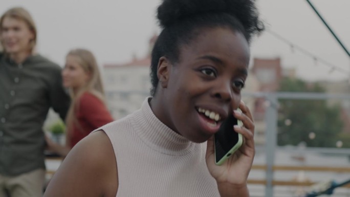 年轻的非洲裔美国妇女在屋顶派对上用手机大声喊叫