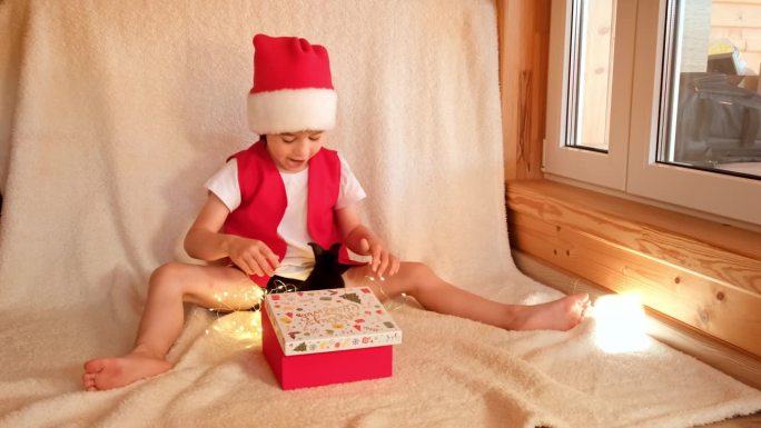 穿着圣诞老人服装的小男孩打开装有黑兔子的礼盒，高兴极了。童年与宠物的爱。圣诞快乐。兔是中国农历202