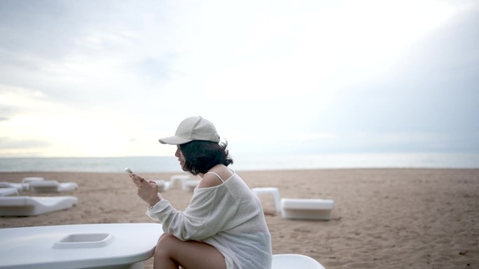 日出时，年轻的亚洲女子在海边玩手机。