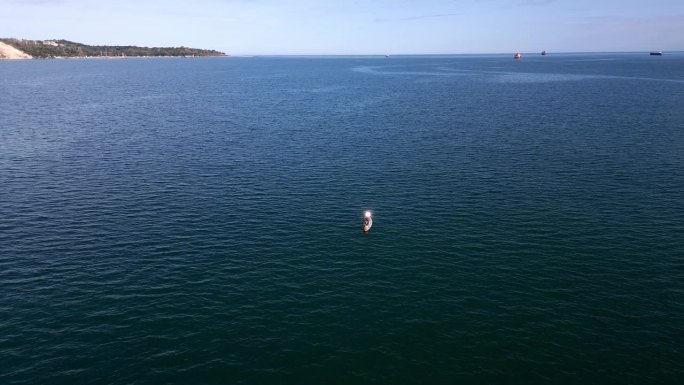 在开阔的海面上，一名男子在冲浪板上用信号镜发出求救信号