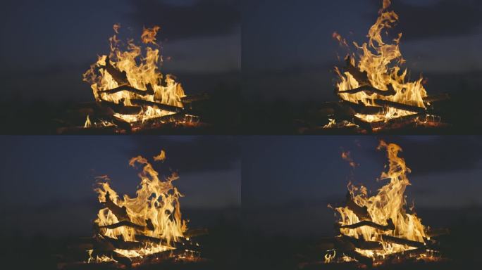 篝火在深蓝色天空背景上的慢动作镜头。橙色的火焰在夜晚的营火。干树枝在火中燃烧