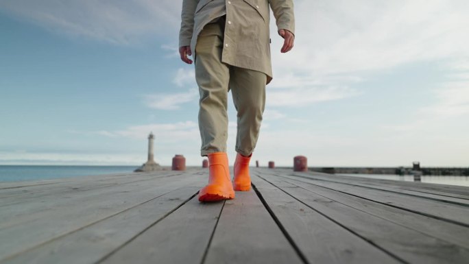 清晨，穿着亮橙色胶靴的渔夫走在古老的木制码头上，看着男人的腿