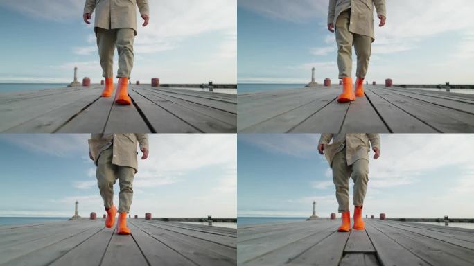 清晨，穿着亮橙色胶靴的渔夫走在古老的木制码头上，看着男人的腿