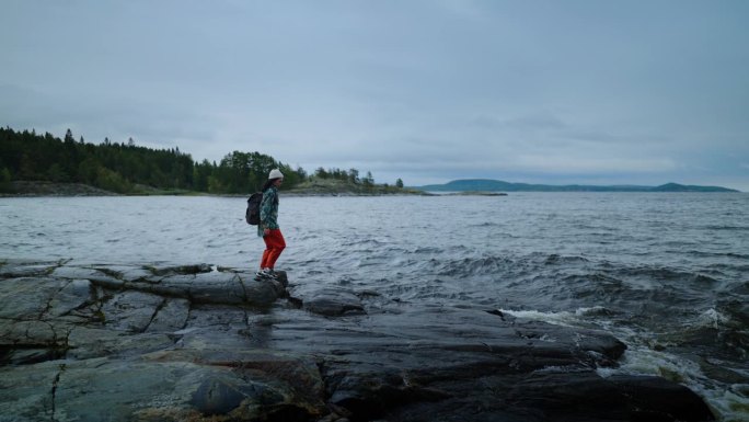 秋日漫步大自然，一位穿着运动服背着背包的女子漫步在石岸湖畔