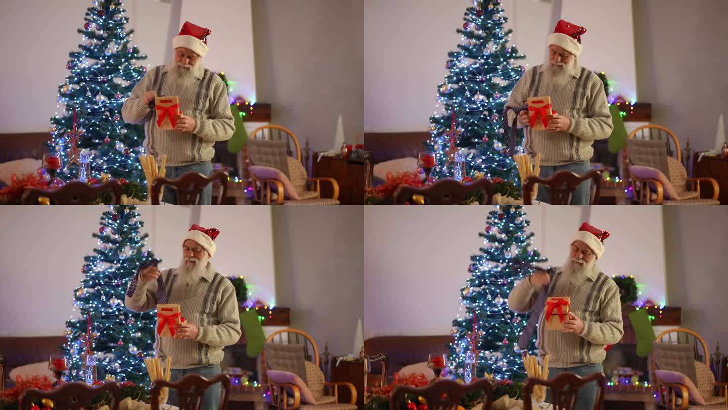 一位留着胡子、头戴圣诞帽的老人站在圣诞树旁，从礼物中取出一条男士领带，试了试。