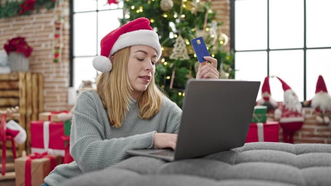 年轻的金发女人买笔记本电脑和信用卡在家里庆祝圣诞节