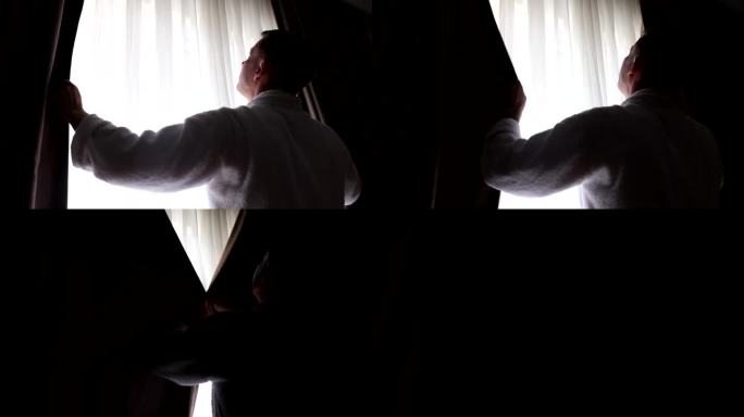 男人站在窗前，用手拉上窗帘