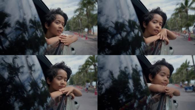 亚洲可爱的小男孩，满是幸福的笑脸，看着打开的车窗外的车辆沿着道路巡游。