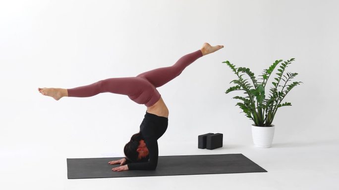 一名女子在练习瑜伽，在垫子上穿着运动服练习腰式和腰式，肘部站立和纵向分开，倒立体式