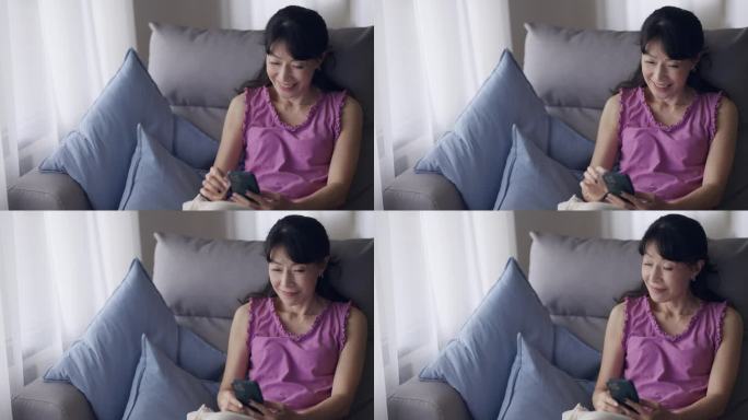 一位中年妇女正躺在客厅的沙发上玩智能手机。