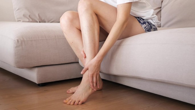 一个年轻的女孩在漫长的一天工作后在家按摩她又细又长又累的腿。预防静脉曲张。