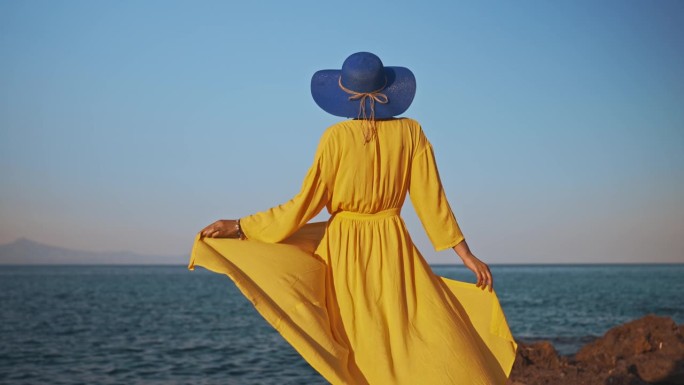 身穿黄色连衣裙的女人对着大海。