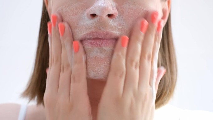 年轻女子用洁面泡沫洗脸(特写，白色背景)。