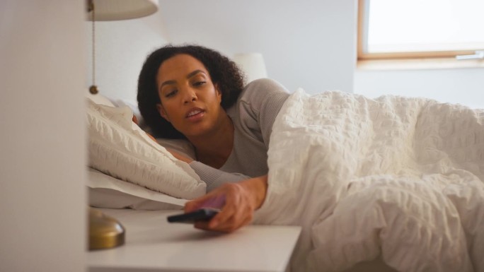 在家躺在床上的女人把手机闹钟关掉了