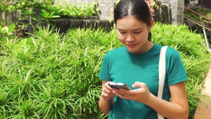 亚洲女人在绿树成荫、流水淙淙的花园里玩手机