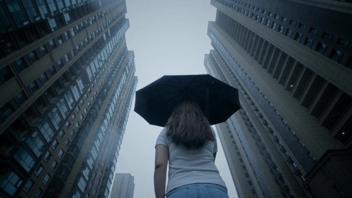 打着伞的女人站在雨中仰望摩天大楼