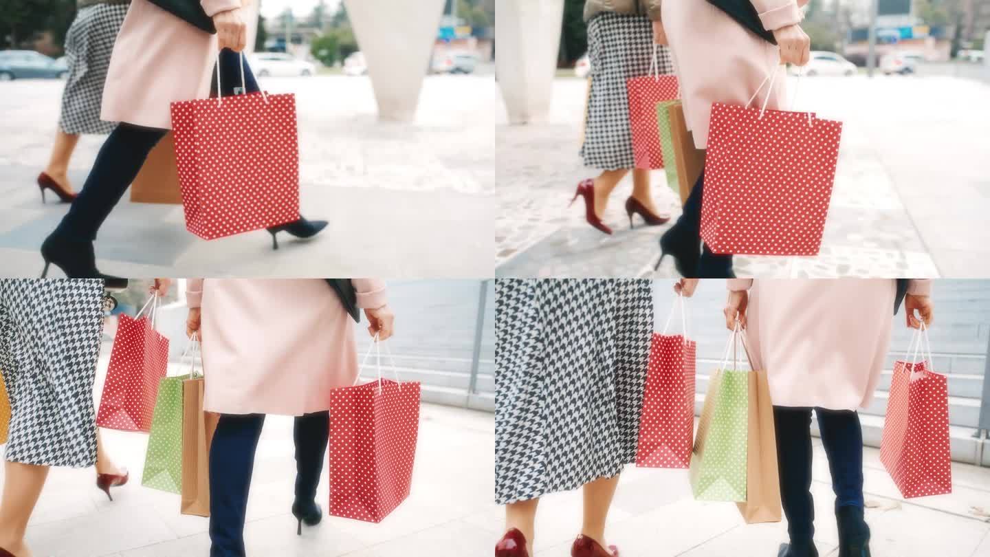 两个面目全非的女人穿着细高跟鞋拎着购物袋走在城市的步行区