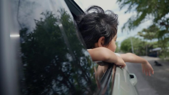 夏日里，可爱的小男孩坐在车里，把脸和手伸出车窗。