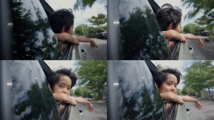 夏日里，可爱的小男孩坐在车里，把脸和手伸出车窗。