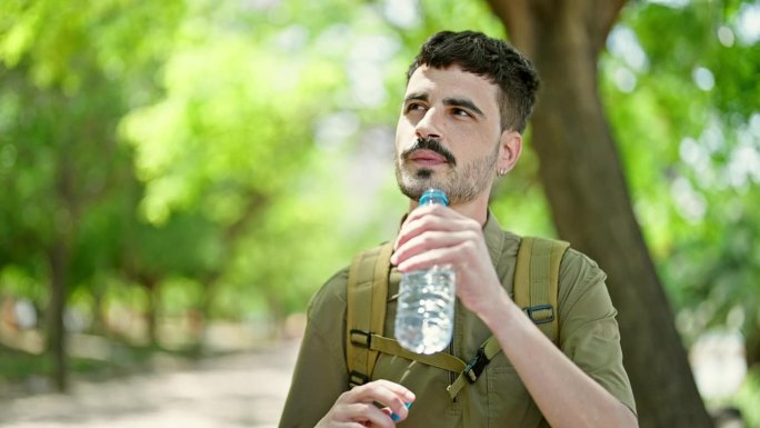 年轻的西班牙裔游客背着背包在公园喝瓶装水