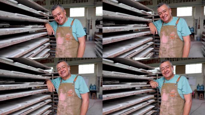 一个陶瓷厂欢快的工匠的视频肖像，他把胳膊肘靠在架子上，面带微笑