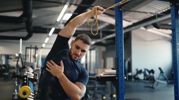 身穿运动服的肌肉男运动员在健身房用健身橡皮筋做伸展运动