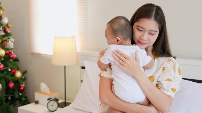 年轻的亚洲母亲抱着孩子在卧室里睡觉。快乐的妈妈正在和她的宝宝拥抱和交谈。母亲节的概念。