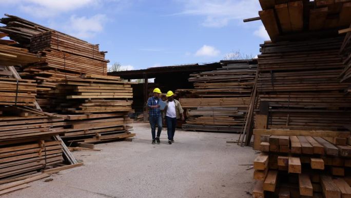 一队工人走过木材场，指着一些需要运往客户的木材