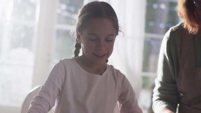 小女孩和奶奶在圣诞节准备烤姜饼的慢动作肖像。可爱的小女孩帮助她的奶奶做家务和做饭，一起过节
