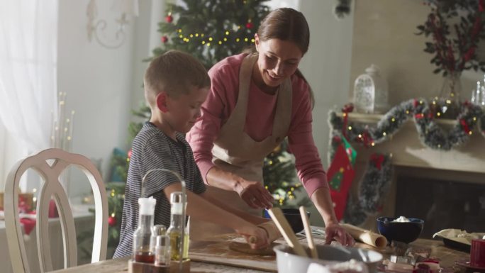 乐于助人的小儿子和他的妈妈准备面团和制作姜饼饼干。快乐的童年假期回忆。在冬天的圣诞节，母亲和孩子一起