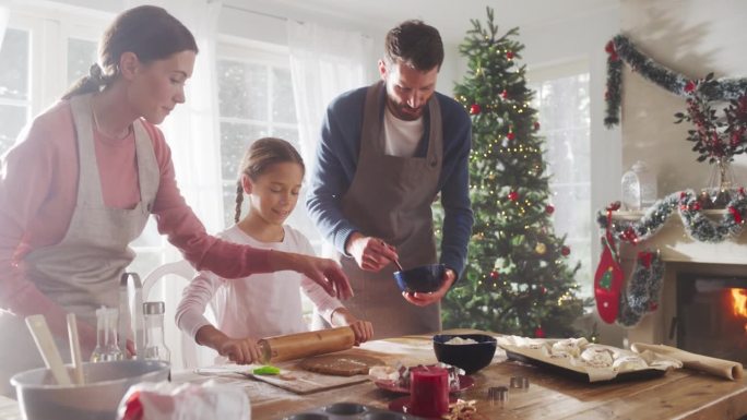 圣诞节快乐的家庭:可爱的小女孩学习如何制作饼干，并与父母一起庆祝她的成就的慢动作肖像。可爱的一家人一