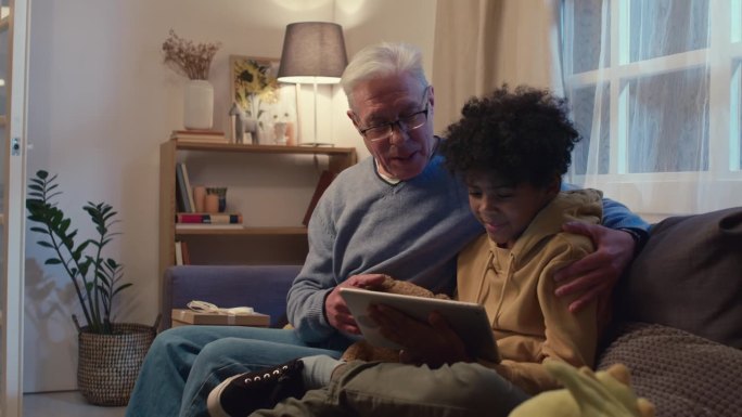 爷爷和孙子坐在沙发上一起看平板电脑