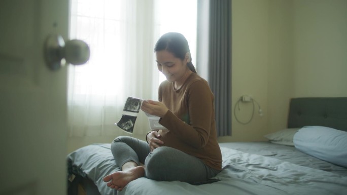 孕妇坐在沙发上看着超声波图像，摸着肚子