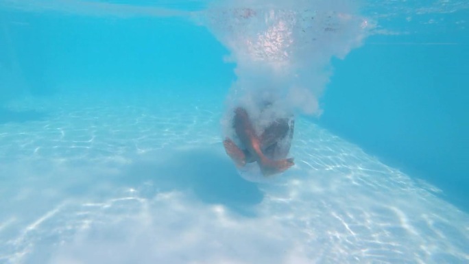水下镜头:不知名的男性跳入游泳池并坐在池底。一个男人在炎热的夏日享受茶水，在温泉或酒店游泳的跟踪镜头