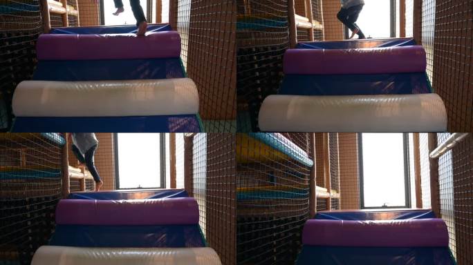 一个男孩在酒店的操场上玩耍，他在彩色垫子上爬，慢动作的场景