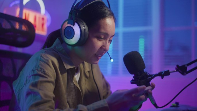 快乐的亚洲女性玩家戴着耳机比赛，用智能手机在线玩视频游戏
