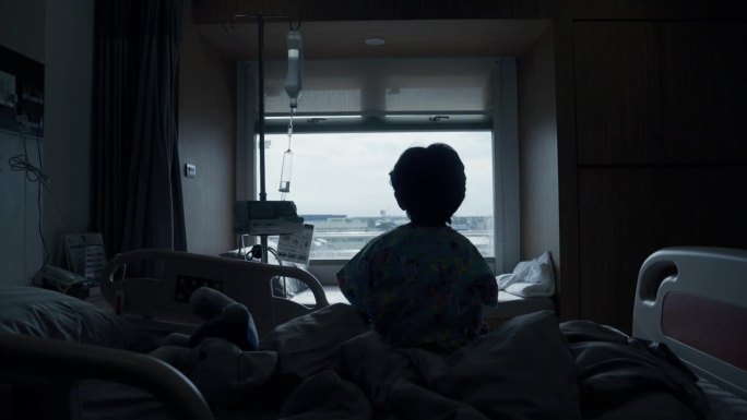 孩子的剪影照片是生病和无聊，他坐在床上，看着窗外。