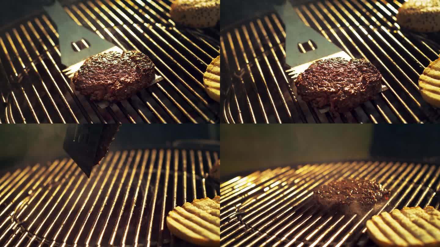 一个人准备汉堡的特写。美味的牛肉饼在火焰烤架上烤，用不锈钢铲翻转肉。电影超级慢动作镜头与速度斜坡效果