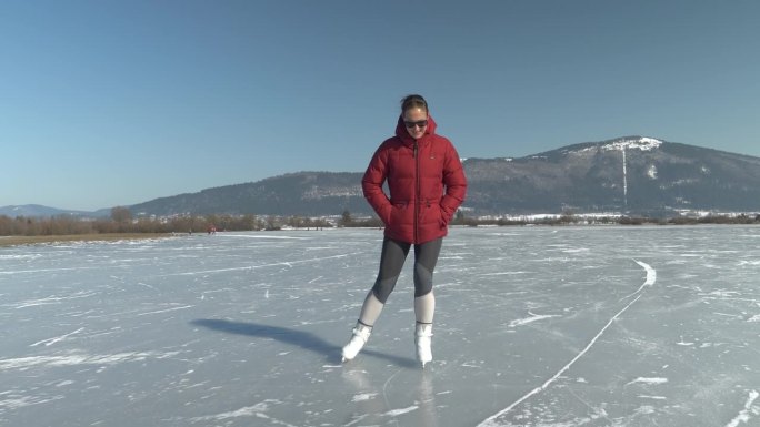 在一个阳光明媚的冬日，微笑的年轻女士在结冰的湖面上滑冰