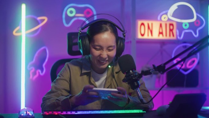 快乐的亚洲女性玩家戴着耳机比赛，用智能手机在线玩视频游戏