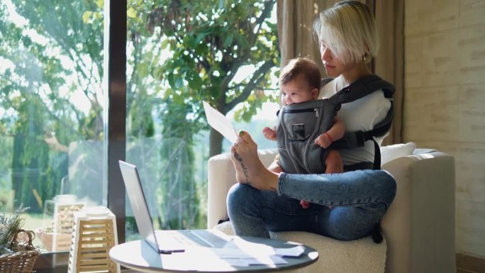 一位天生没有手臂的母亲把孩子抱在婴儿背带里，一边用脚拿着账单，一边用笔记本电脑上网支付账单。一名患有