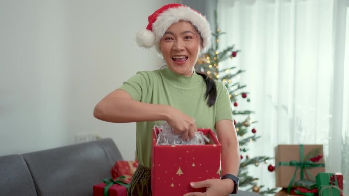亚洲女人开心地打开礼盒，对着镜头扔碎纸屑。圣诞节的有趣时刻。